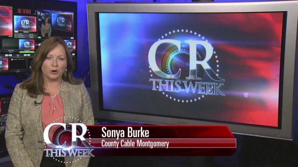 A still from a segment with one of the hosts of County Report This Week, with a TV screen behind her.